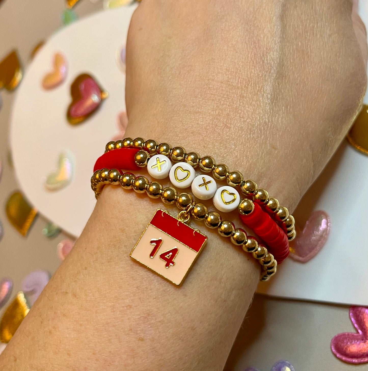 Love Stack 3: Two gold plated bead stretch bracelets, one with a 14th on the calendar charm and a red clay beaded bracelet with letter beads