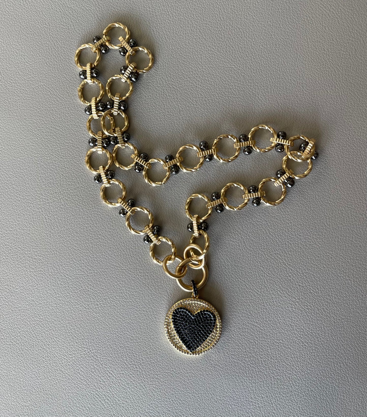 Heart On Your Sleeve Necklace: Brushed gold chain with gunmetal accents, a push gate circle clasp and pavé heart pendant